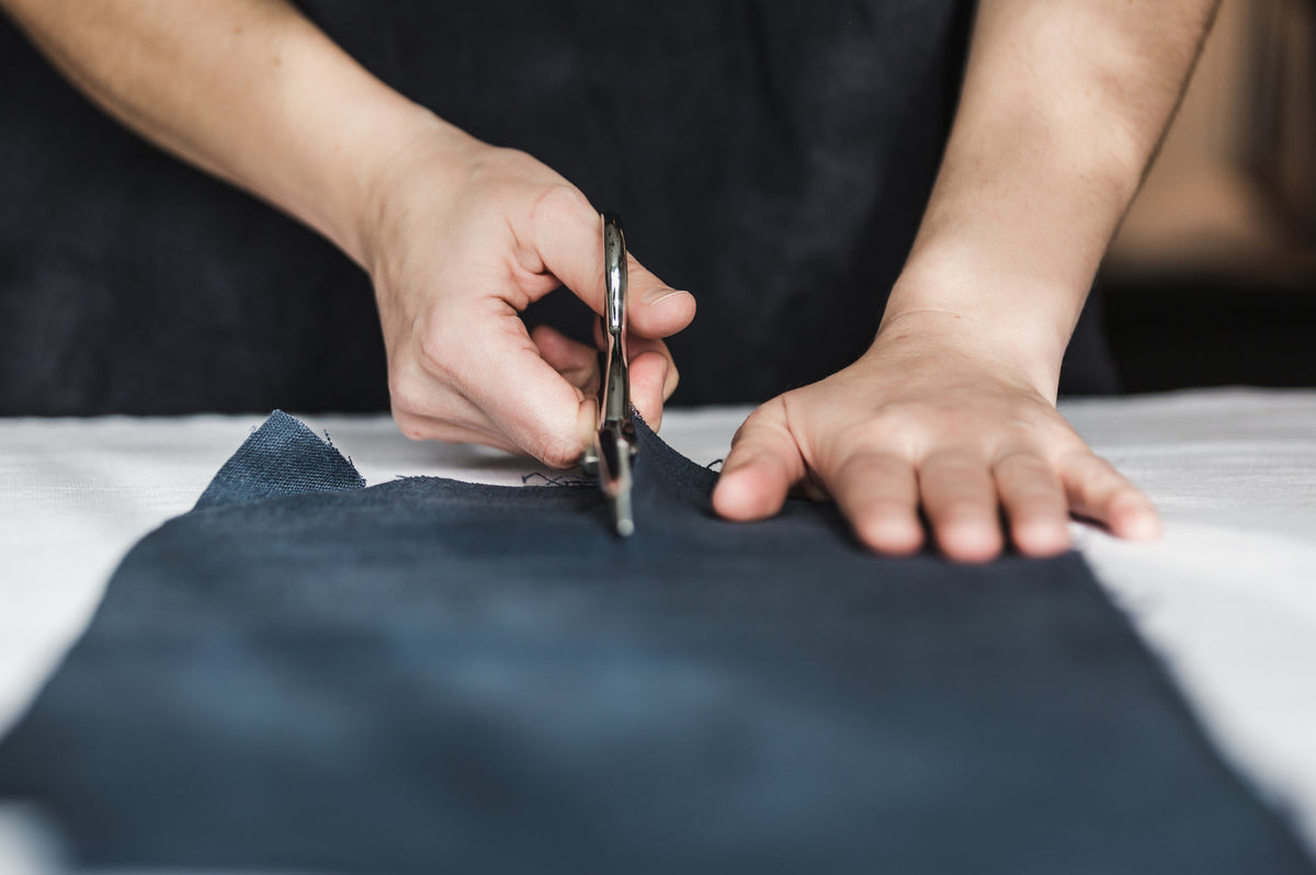 close up of a person using metal fabric scissors to cut through a strip of dark fabric