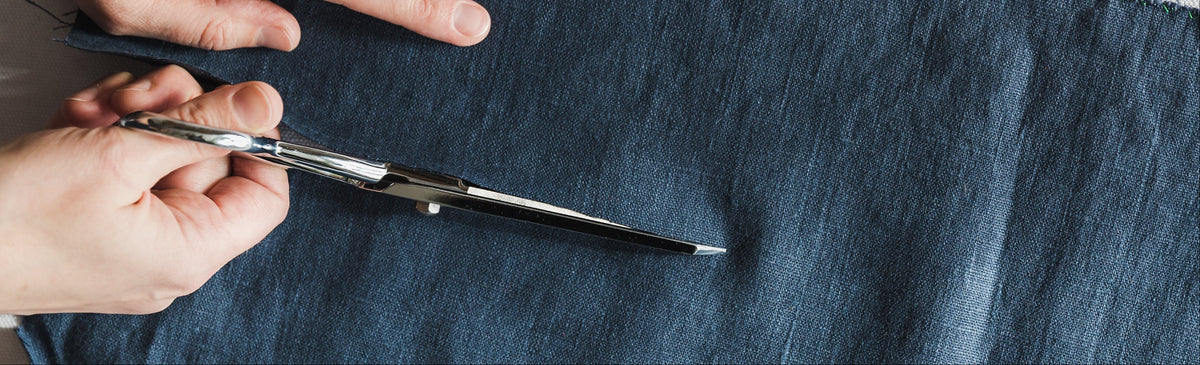 A close up of a person using a pair of fabric scissors to cut through a piece of denim fabric.