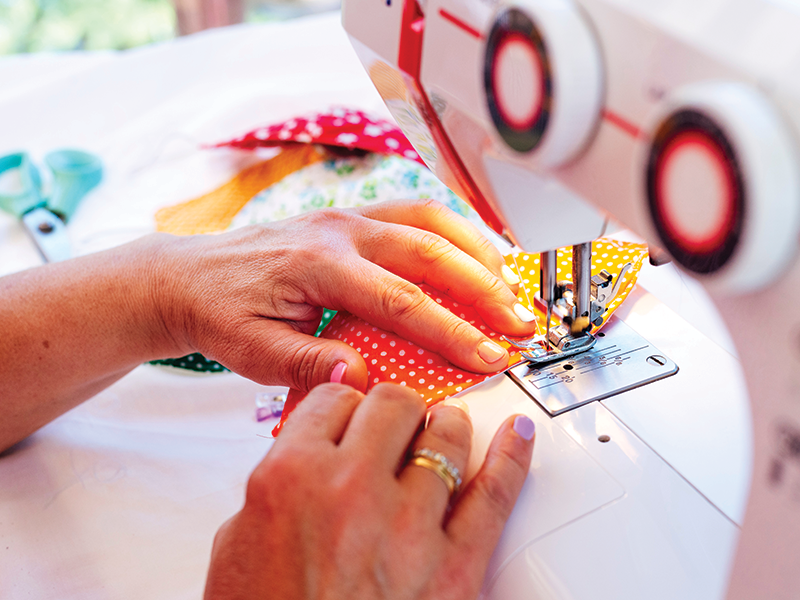 Close up of a person's hands pushing a piece of fabric through a sewing machine